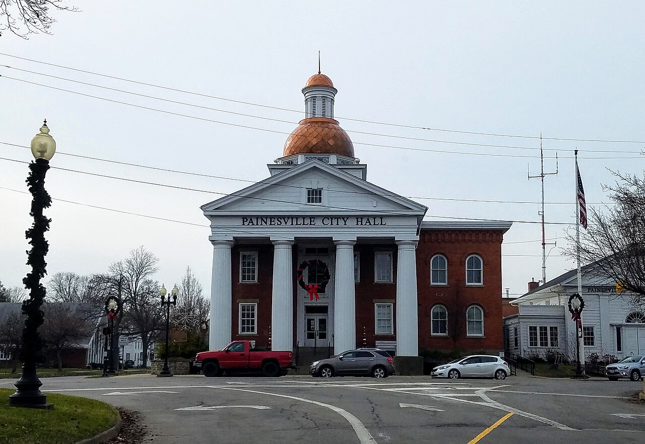 Painesville City Hall, a red brick building with a white-columned portico and a copper dome, seen across the street in Painesville, Ohio