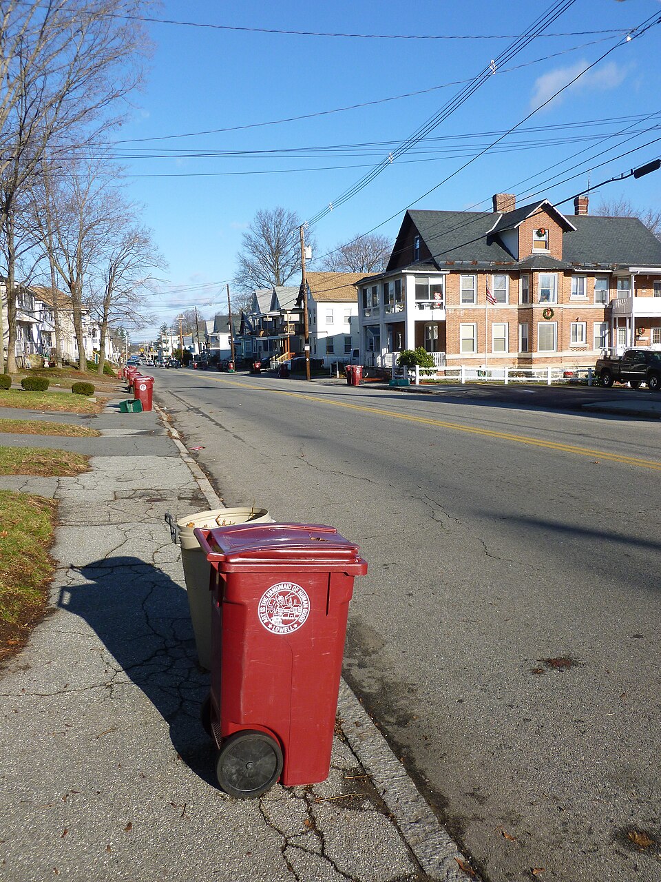 A residential street in Lowell, Massachusetts, in December with a city trash cart at the curb