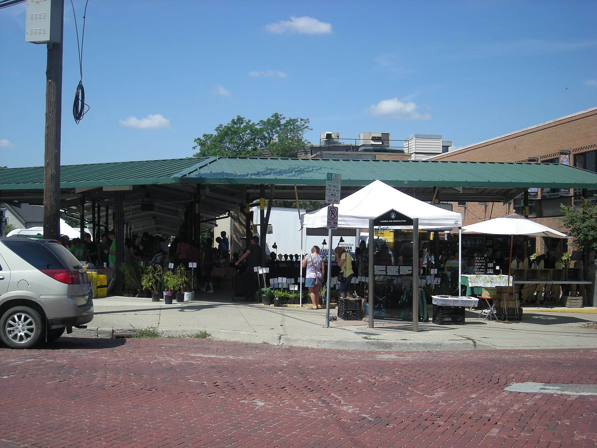Covered stalls of the Ann Arbor Farmers Market seen across a brick street on a summer market day, Ann Arbor, Michigan.