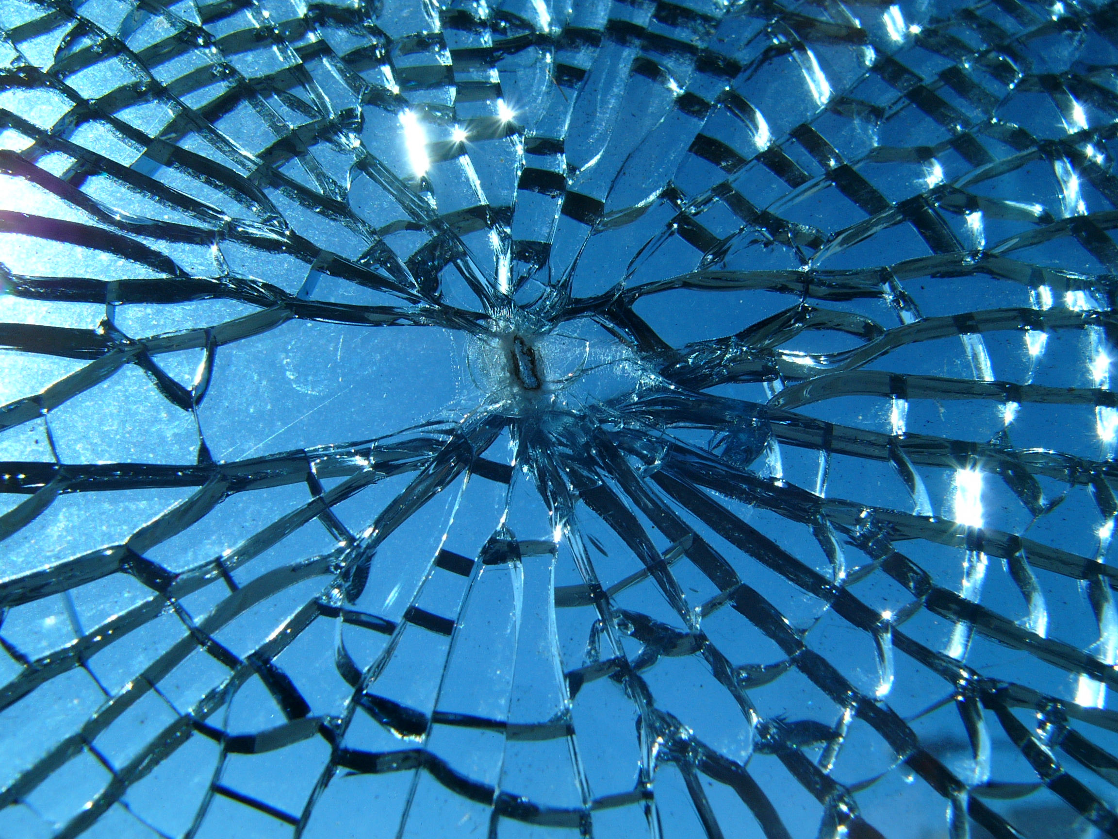 Close-up of blue glass fractured into many pieces around a central impact point.