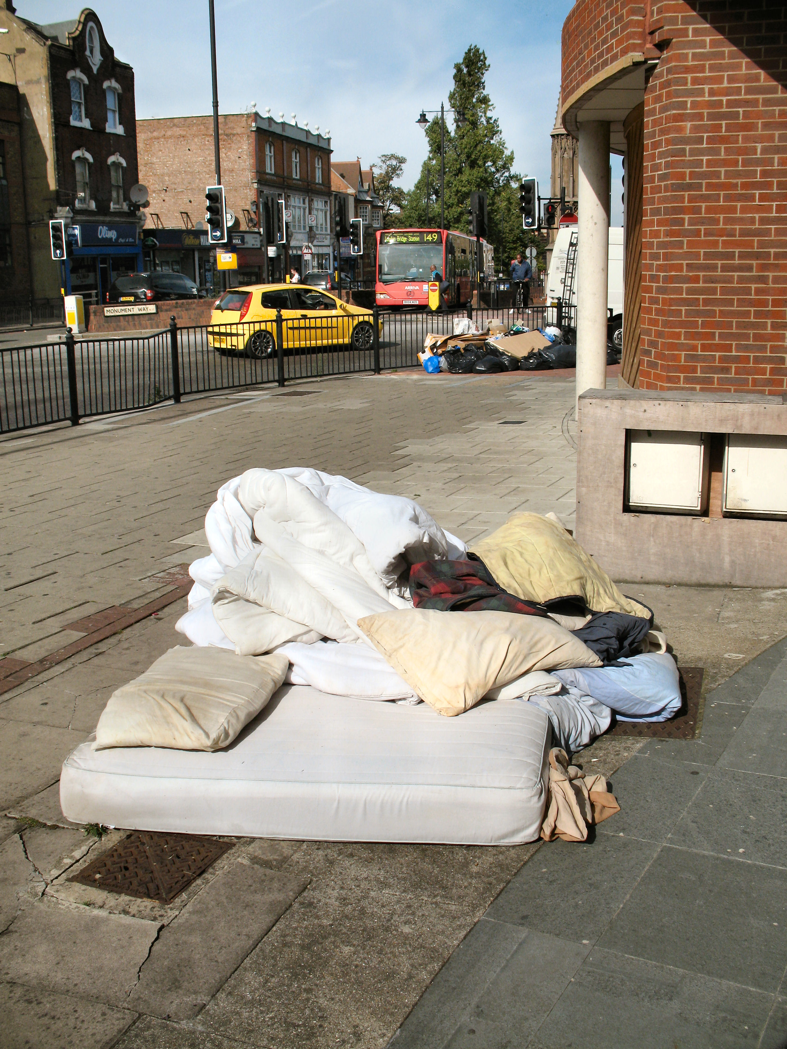 A discarded mattress, bedding and bags piled on a city sidewalk A discarded mattress, bedding and bags piled on a city sidewalk