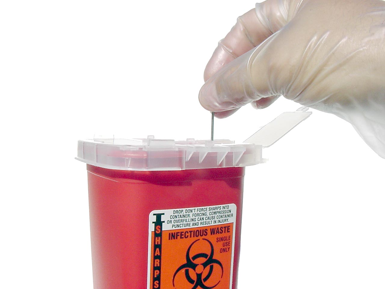 A gloved hand dropping a sharp into a red sharps container.