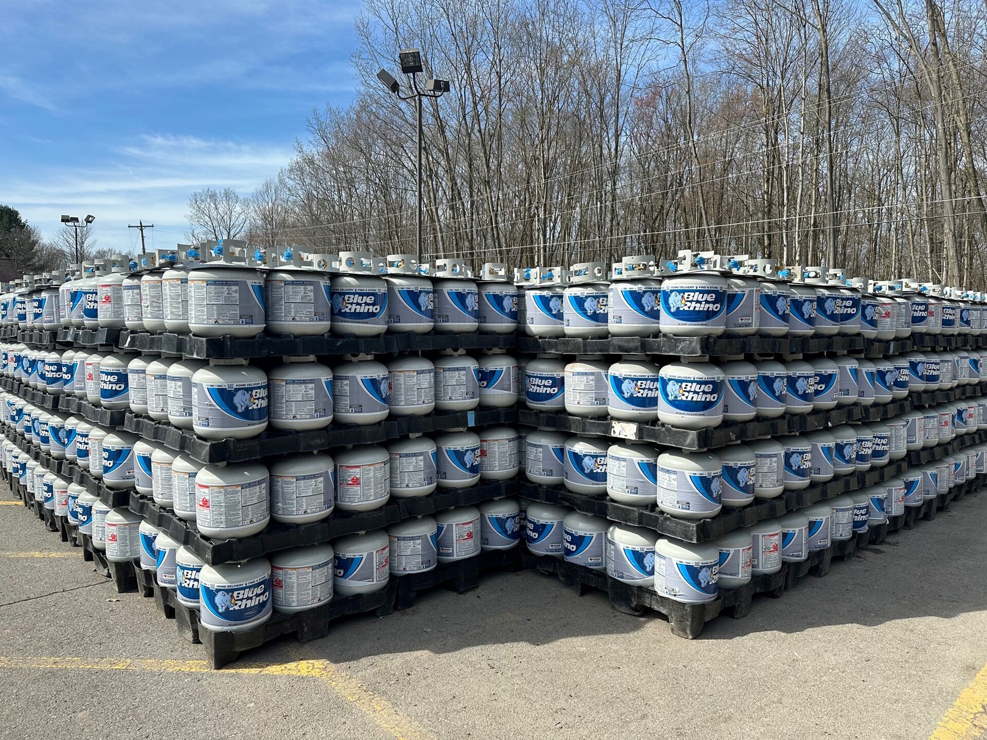 Stacks of Blue Rhino propane grill tanks on black pallets in a parking lot in Grove City, Pennsylvania