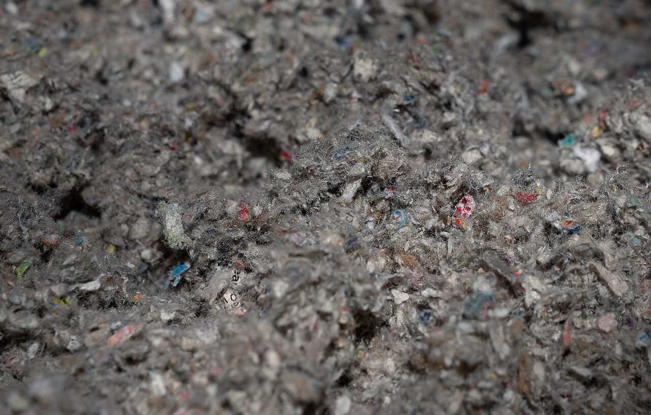 Close-up of finely shredded post-consumer paper fibers in grey with flecks of colored print