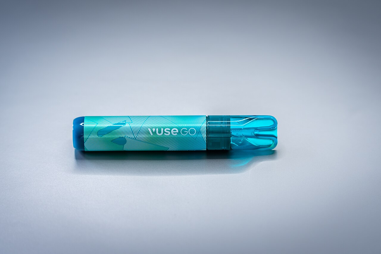 A single teal disposable vape lying on its side on a plain gray surface, mouthpiece to the right